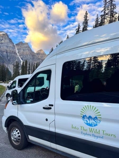 Into the Wild Tours shuttle van parked near Moraine Lake in Banff National Park, offering guided tours and private transfers through the Canadian Rockies.