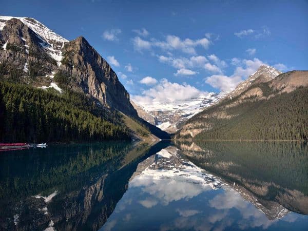 Snow-capped peaks and evergreen forests reflected in the calm waters of Lake Louise, with a bright blue sky above.