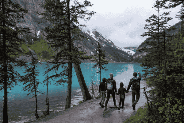 Family walking along Lake Louise shoreline with turquoise water in Banff National Park