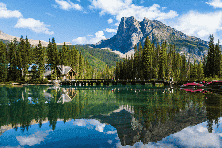 Scenic view of Emerald Lake with mountain reflections, forest shoreline, and the wooden bridge leading to Emerald Lake Lodge.