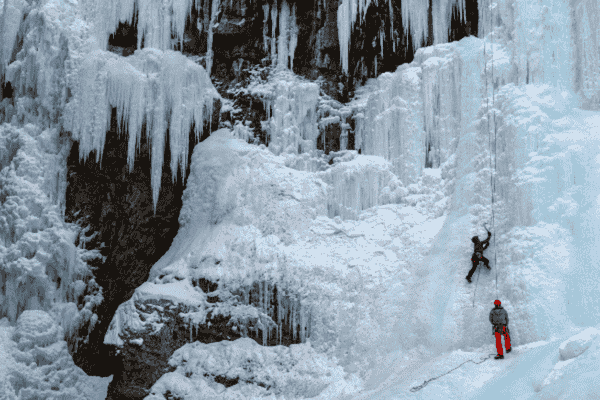 Two climbers scaling the frozen waterfalls of Johnston Canyon, surrounded by dramatic ice formations and rugged cliffs.