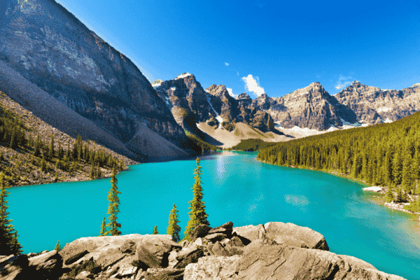Panoramic view of Moraine Lake with vibrant turquoise waters, rocky mountains, and lush green forests.