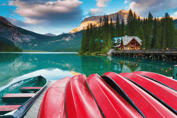 Emerald Lake with red canoes in the foreground, a cozy lakeside lodge, and surrounding forested mountains reflecting on the water.