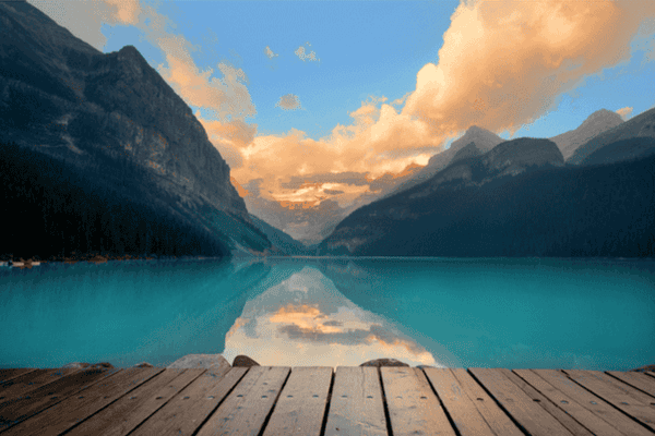 Wooden dock at Lake Louise facing still turquoise water and symmetrical mountain reflections at sunrise