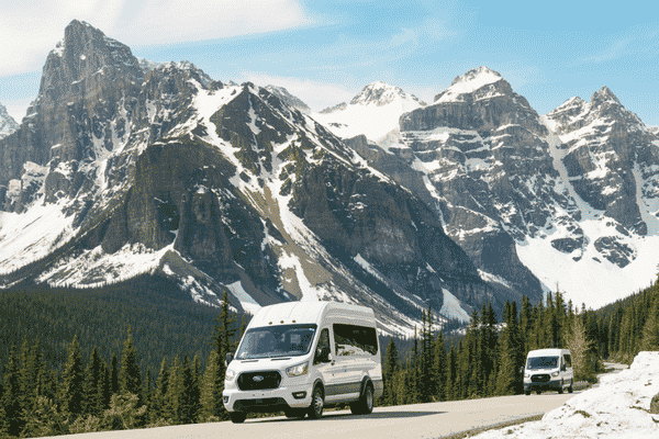 Into the Wild Tours shuttle driving beneath the towering peaks of the Valley of the Ten Peaks near Moraine Lake in Banff National Park.